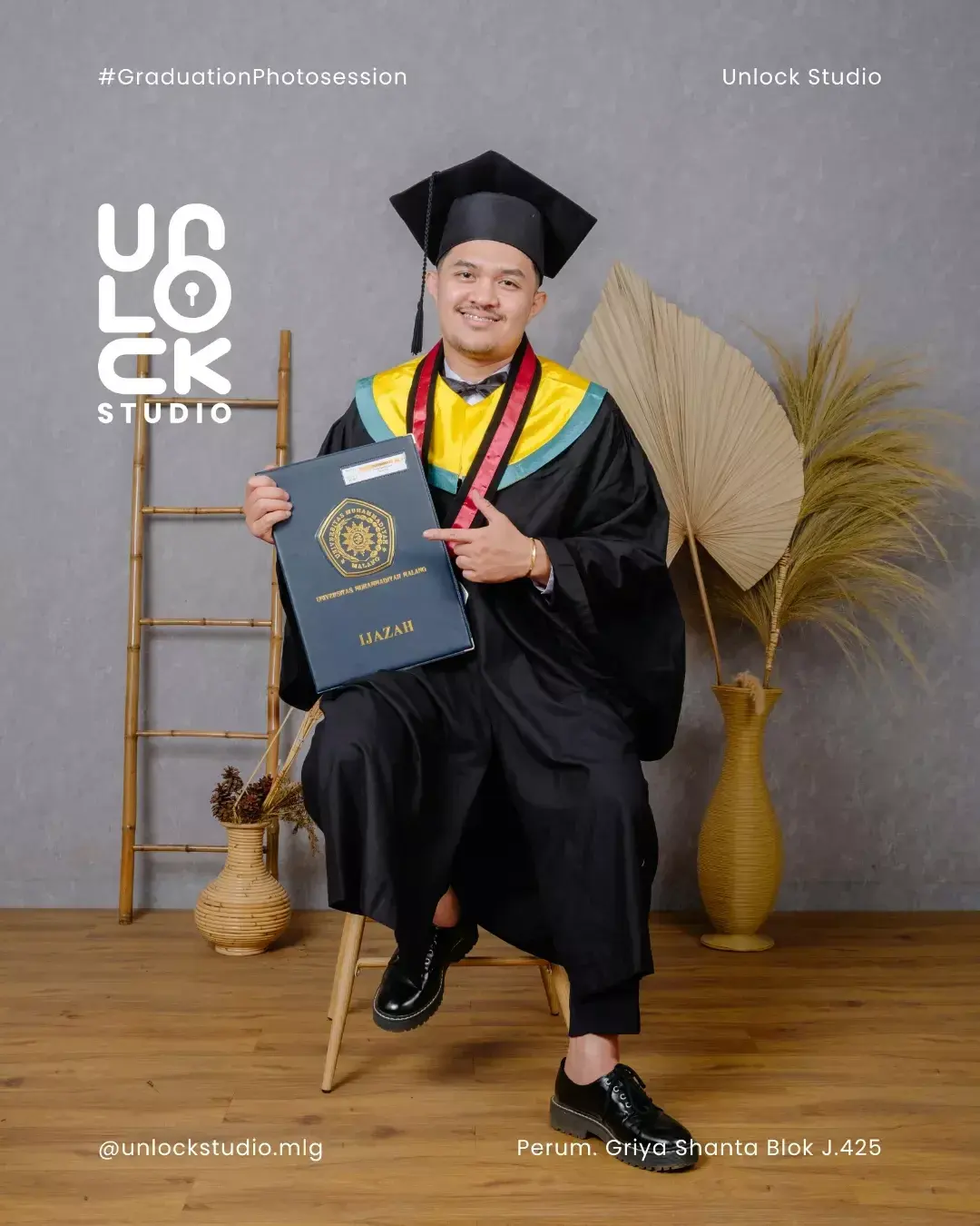 Wisudawan duduk memegang ijazah di studio
